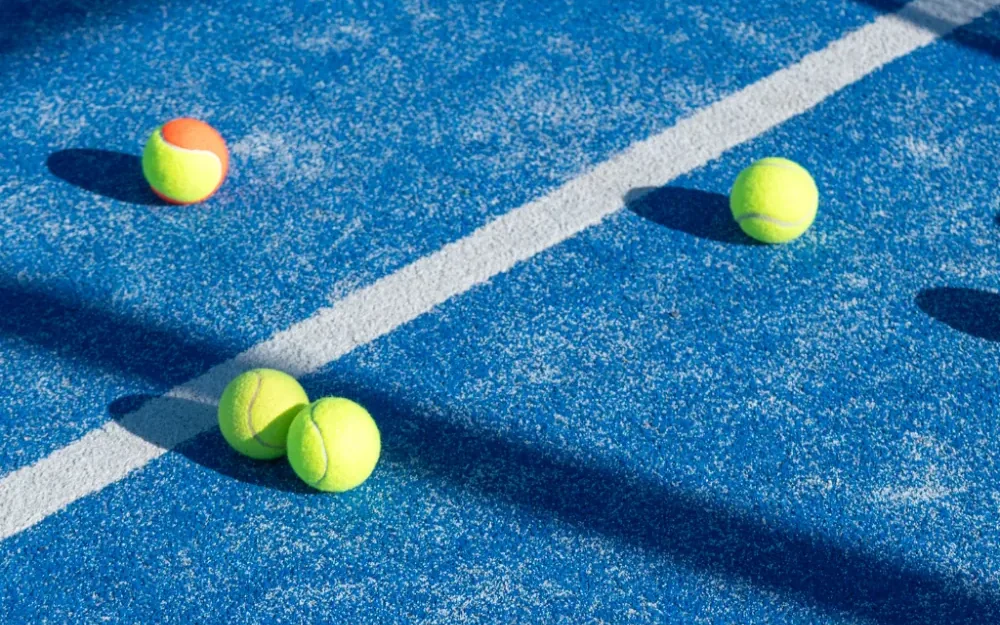 Balles de padel sur le gazon synthétique bleu d'un terrain, ombre du filet · photo d'illustration